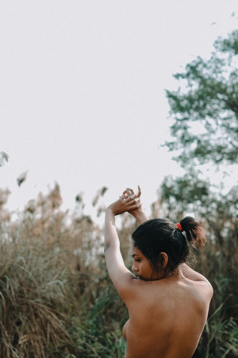 Anonymous naked woman with raised hands near grassy field